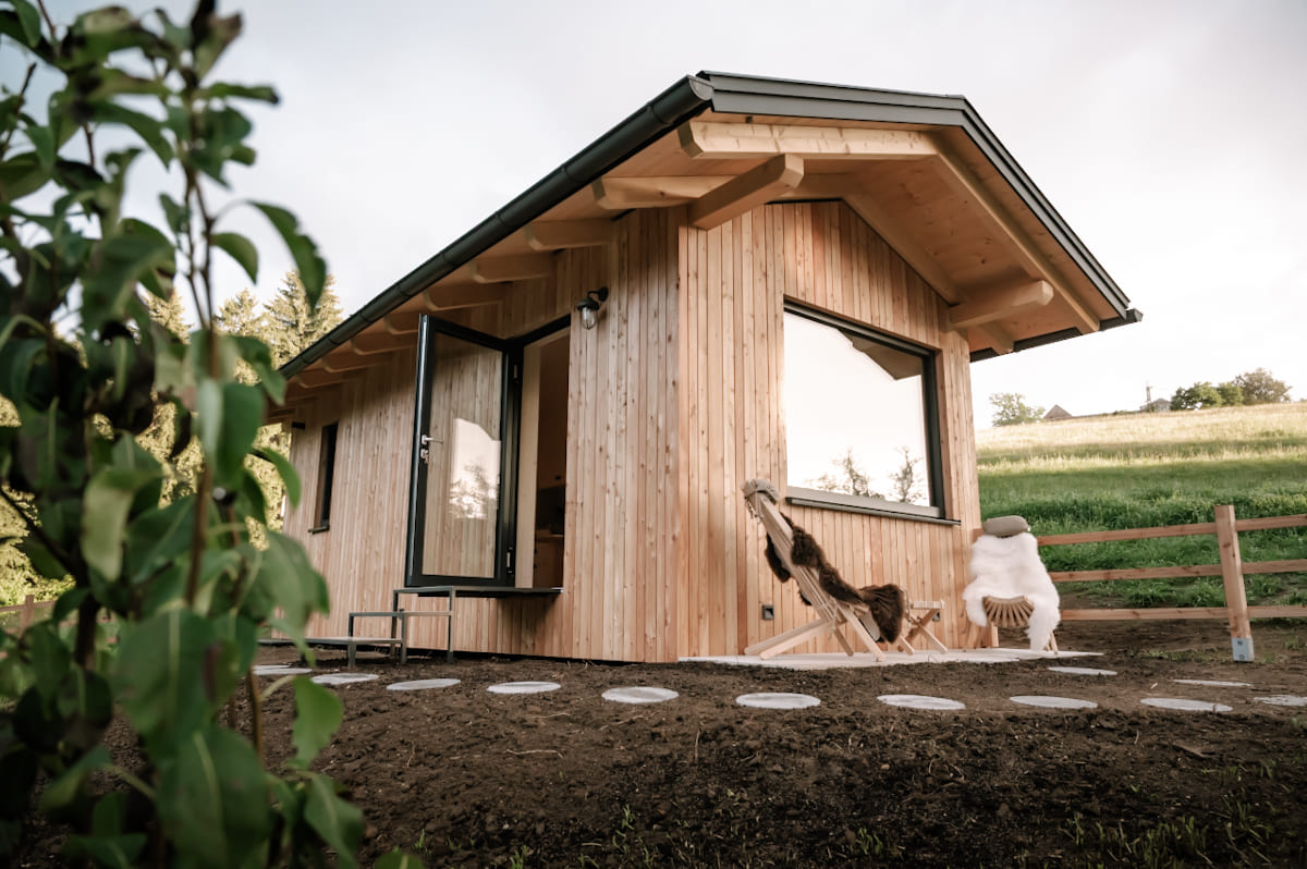 Außenansicht des Tiny Houses Moosgrün im Mostviertel mit einem Gartenbereich, einer Holzbank und einer beeindruckenden Aussicht auf die umliegende Natur.