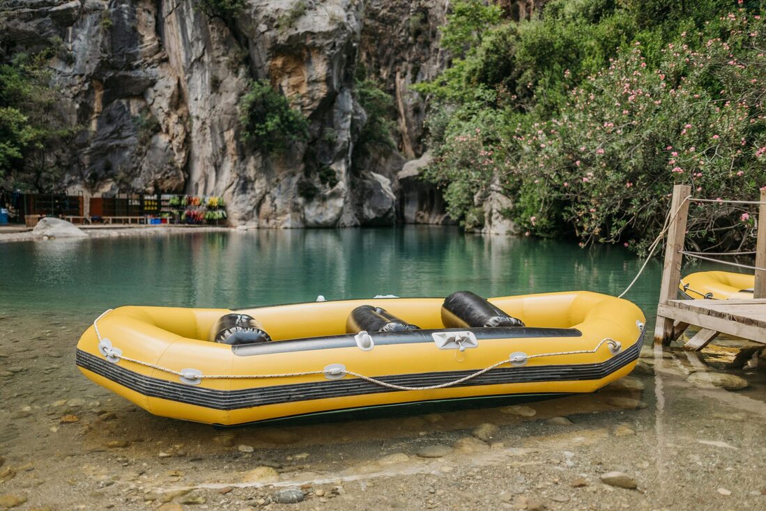 Ein gelbes Rafting Boot liegt an einem ruhigen Fluss. umgeben von hohen Felsen und grünen Pflanzen.